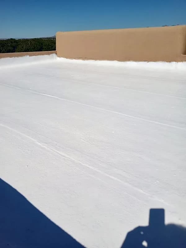 Smooth white coated flat roof meeting a tan stucco parapet under a blue sky