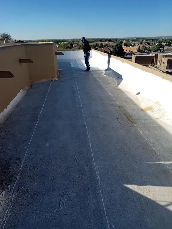 Worker walking a grey flat roof between parapet walls before recoating
