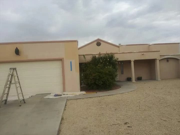The same stucco home mid-job, with a ladder and drop cloths by the garage